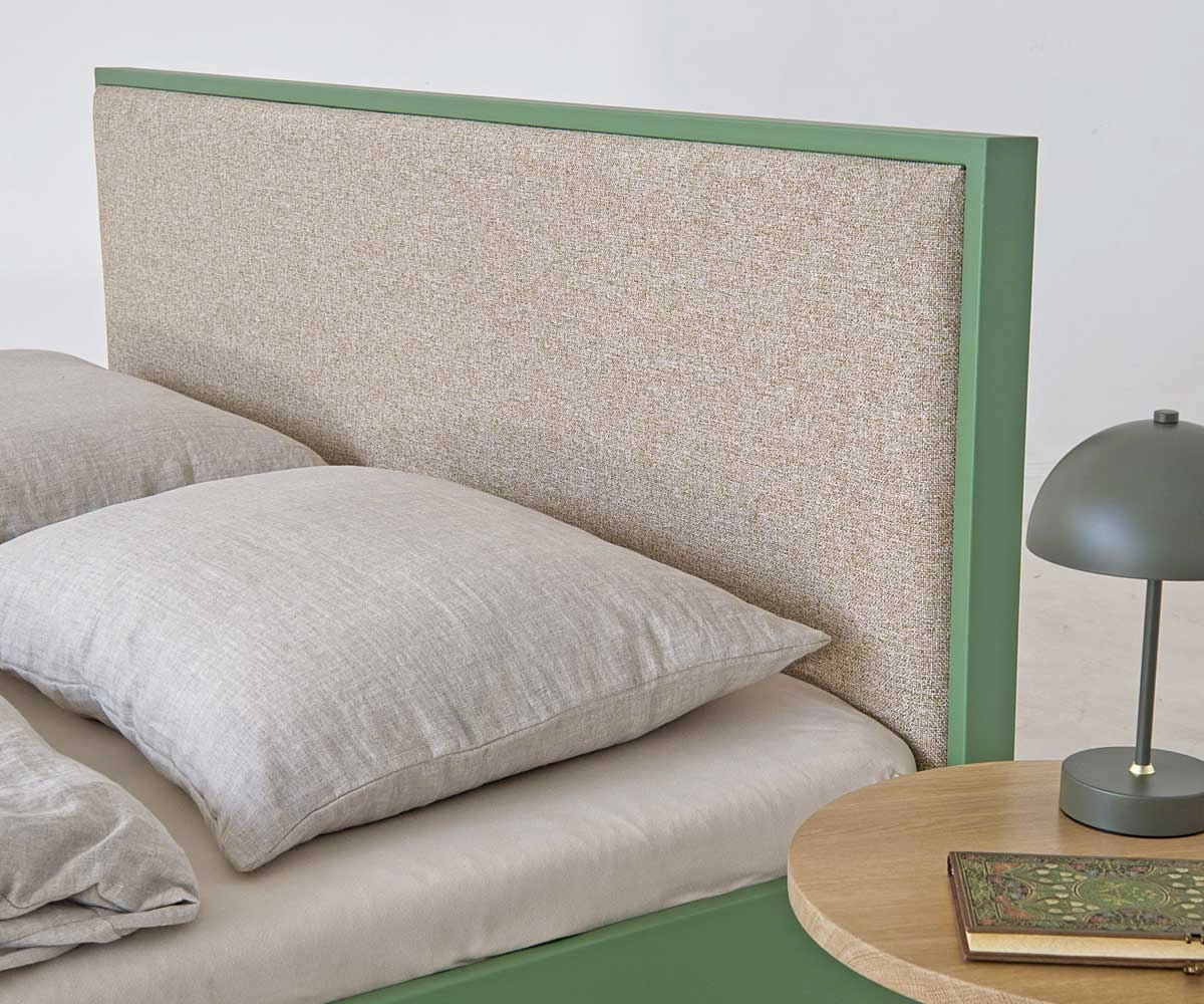 Beige upholstered headboard of modern green metal bed in bedroom