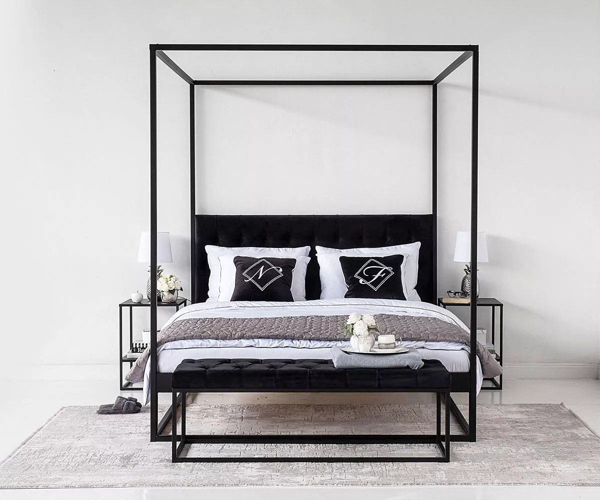 Schwarzes TELA-Himmelbett mit schwarz-weißen Kissen, davor eine schwarze Sitzbank und schwarze Nachttische mit den weißen Nachttischlampen darauf Schwarzes TELA-Himmelbett mit schwarz-weißen Kissen, davor eine schwarze Sitzbank und schwarze Nachttische mit den weißen Nachttischlampen darauf