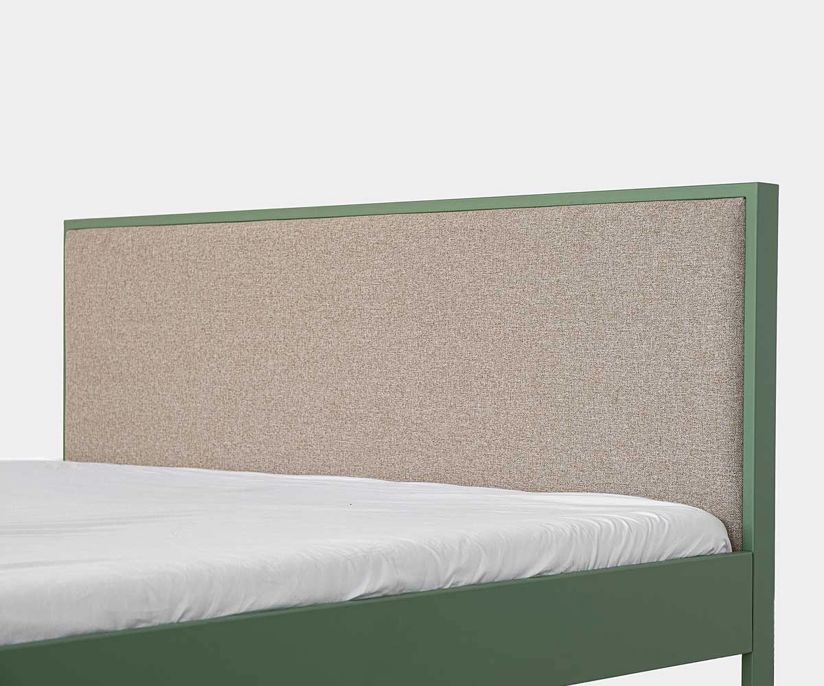 Beige upholstered headboard of a modern green metal bed without footboard